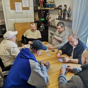 Przy stoliku siedzi  6 osób. W rękach trzymają karty do gry. 